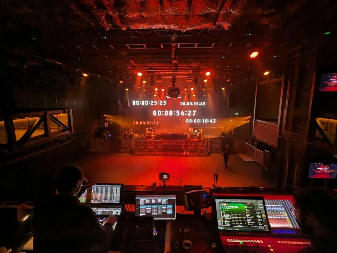 View from front of house over the sound and lighting desks to a club stage with timecode on screen