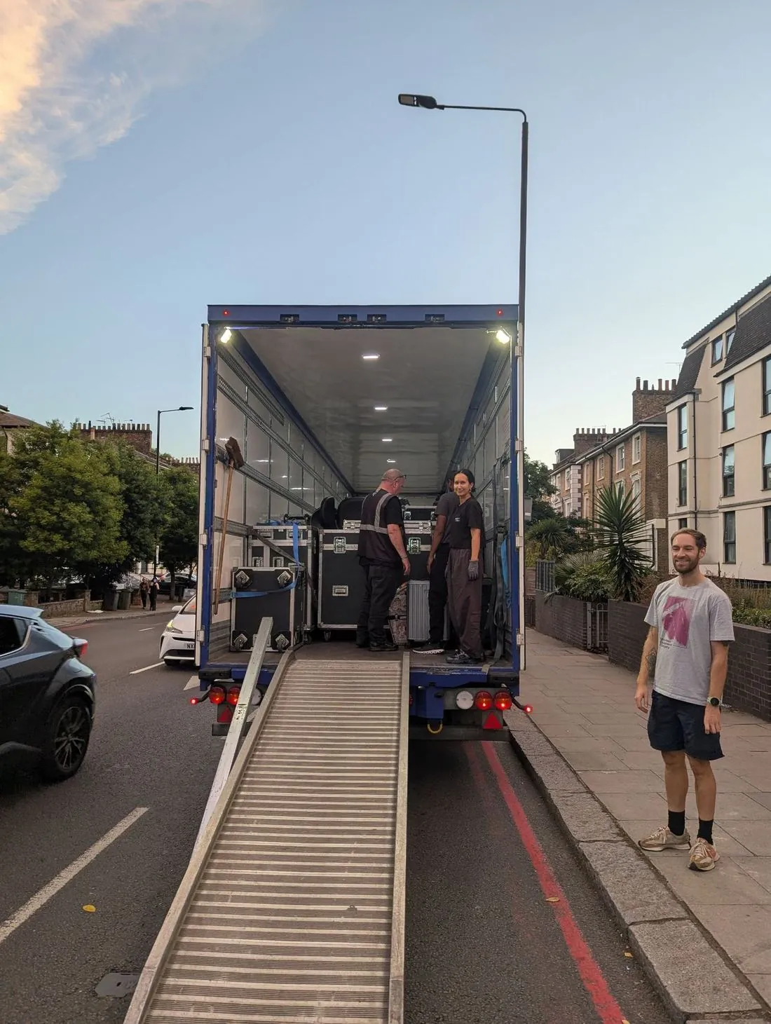 Crew loading flight cases into a trailer on a London street at dusk