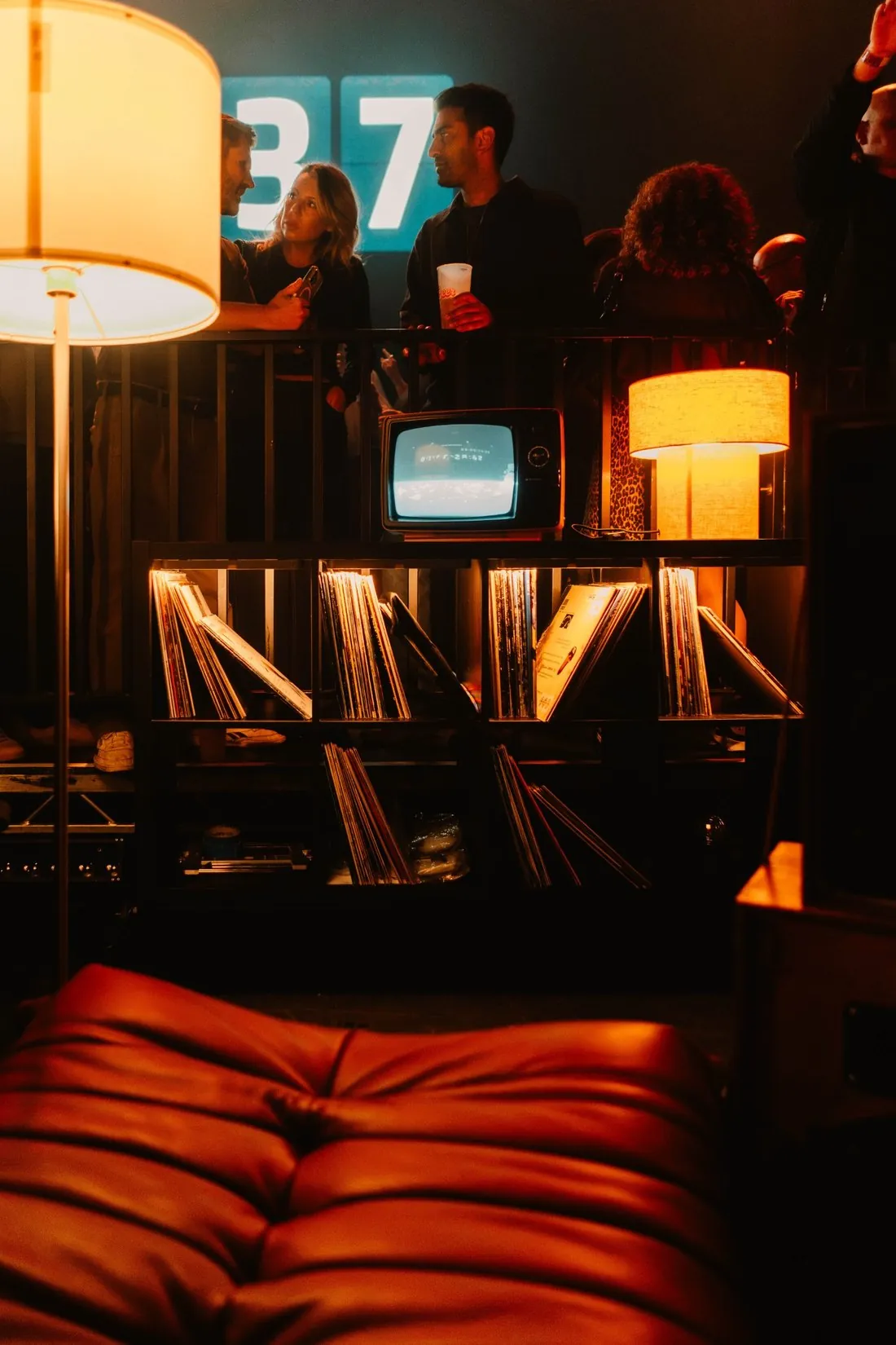 Living-room set dressing beside the stage at Outernet: floor lamp, vintage TV and record shelves