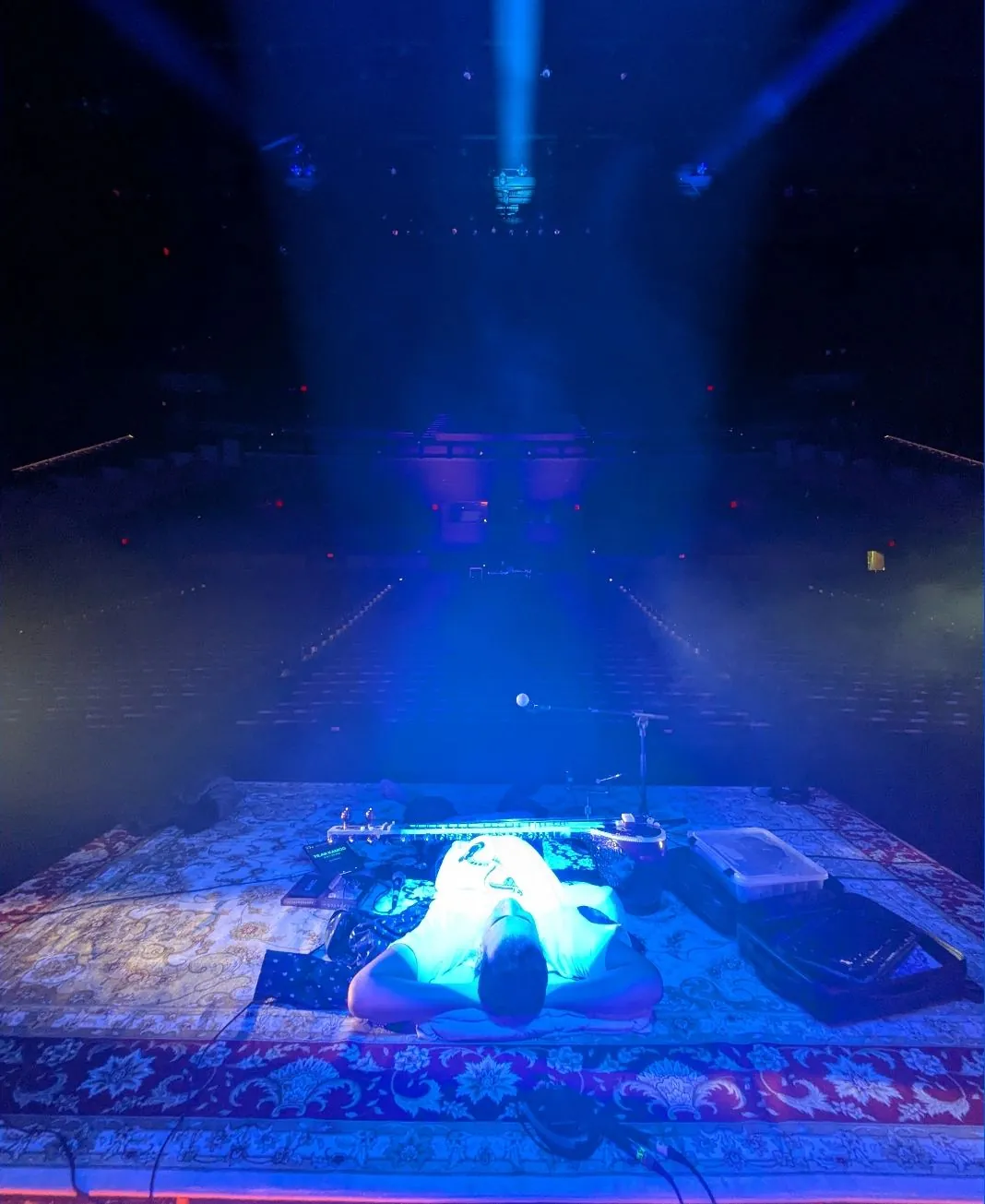 Rishab resting on the stage riser before doors under a single blue beam